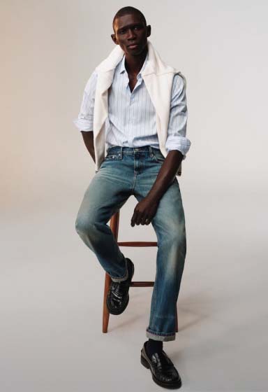 Model wearing a light wash Tommy Hilfiger denim shirt and jeans, standing in a relaxed pose in a studio setting.