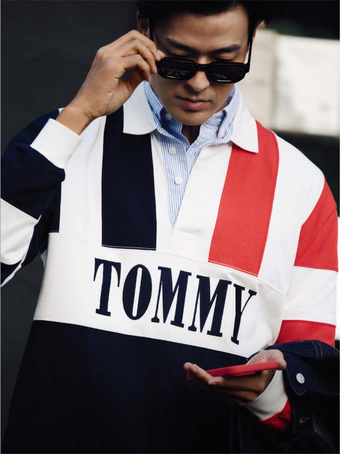 Model in sunglasses while wearing TOMMY branded Tommy Jeans rugby polo.