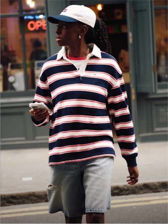 Model wearing stripped Tommy Jeans rugby polo walking down the street.