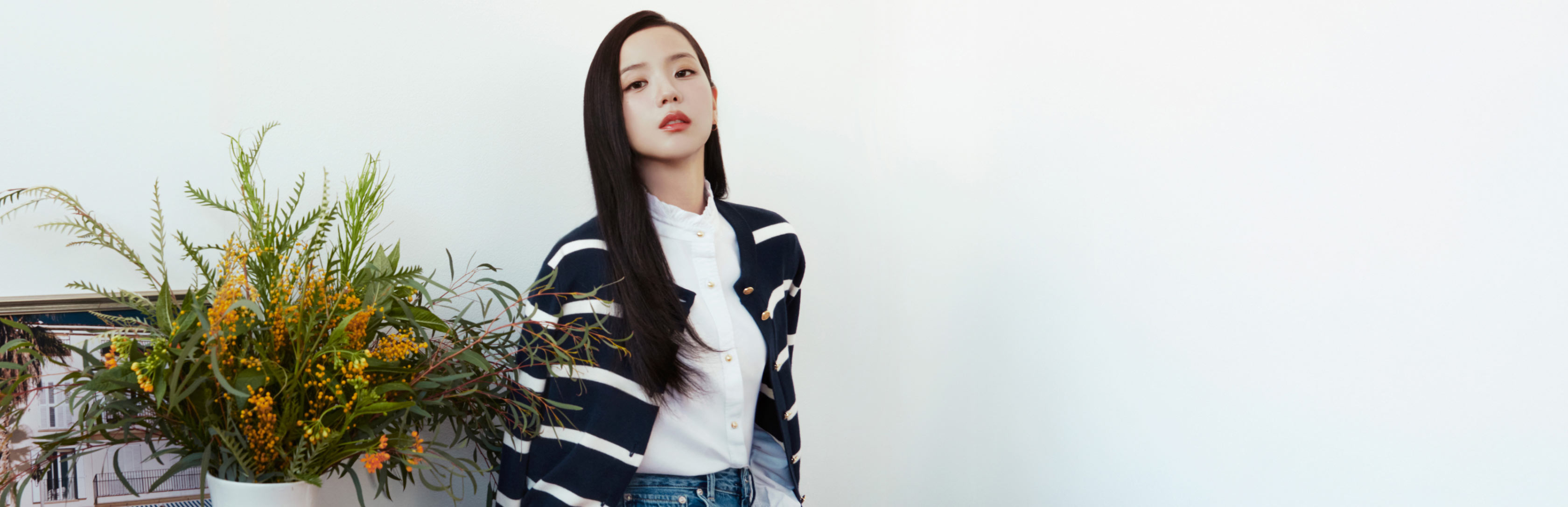 Tommy Hilfiger campaign banner featuring Jisoo in a navy and white patterned sweater, posed beside a floral arrangement on a table.