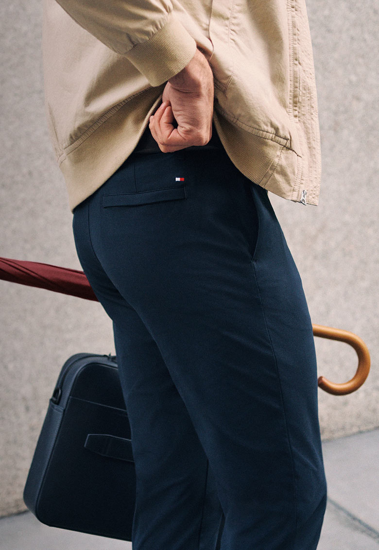 Model outdoors in casual Tommy Hilfiger looks, including a navy jacket layered over a red sweater with beige trousers.