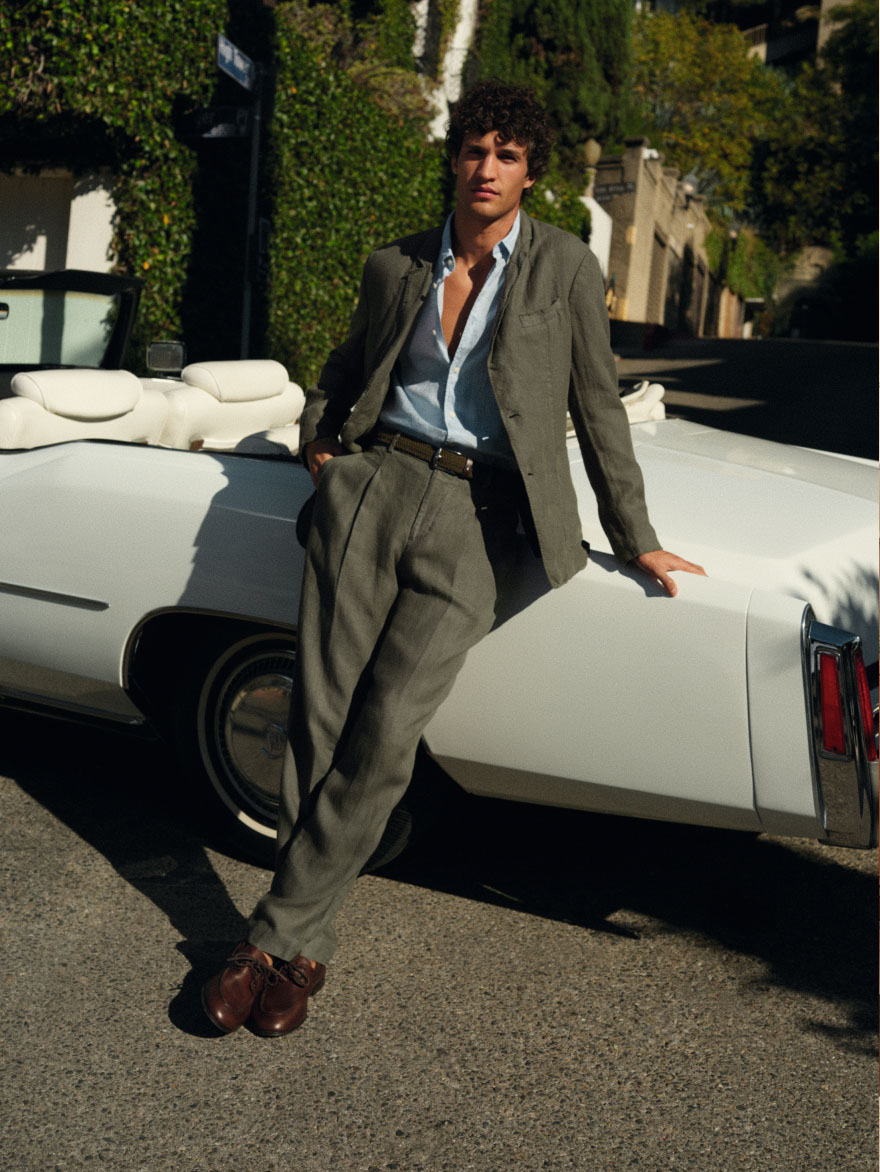 Model leaning on a white convertible wearing a Tommy Hilfiger blazer with wide-leg trousers, styled with a relaxed, dressed-up look.
