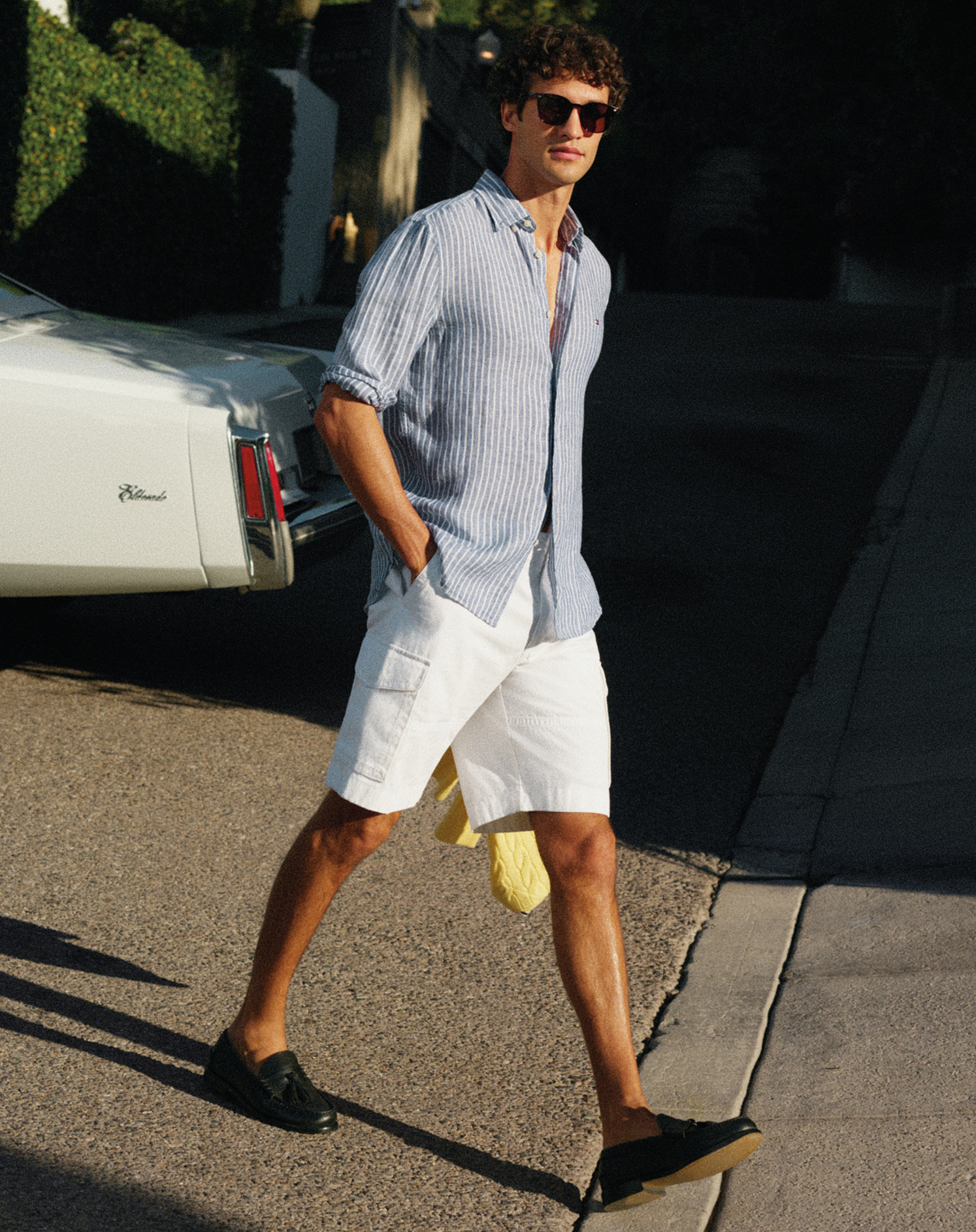 A male model walking outside wearing a Tommy Hilfigershirt and white shorts