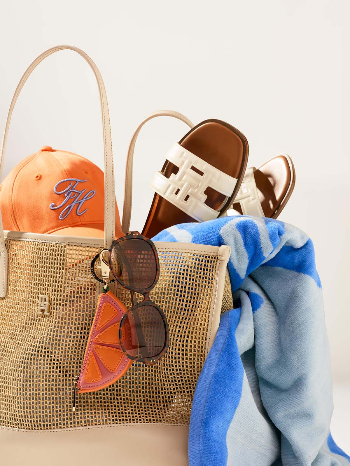 Tommy hilfiger Woven tote bag filled with summer accessories including a cap, sandals, sunglasses, and clothing.