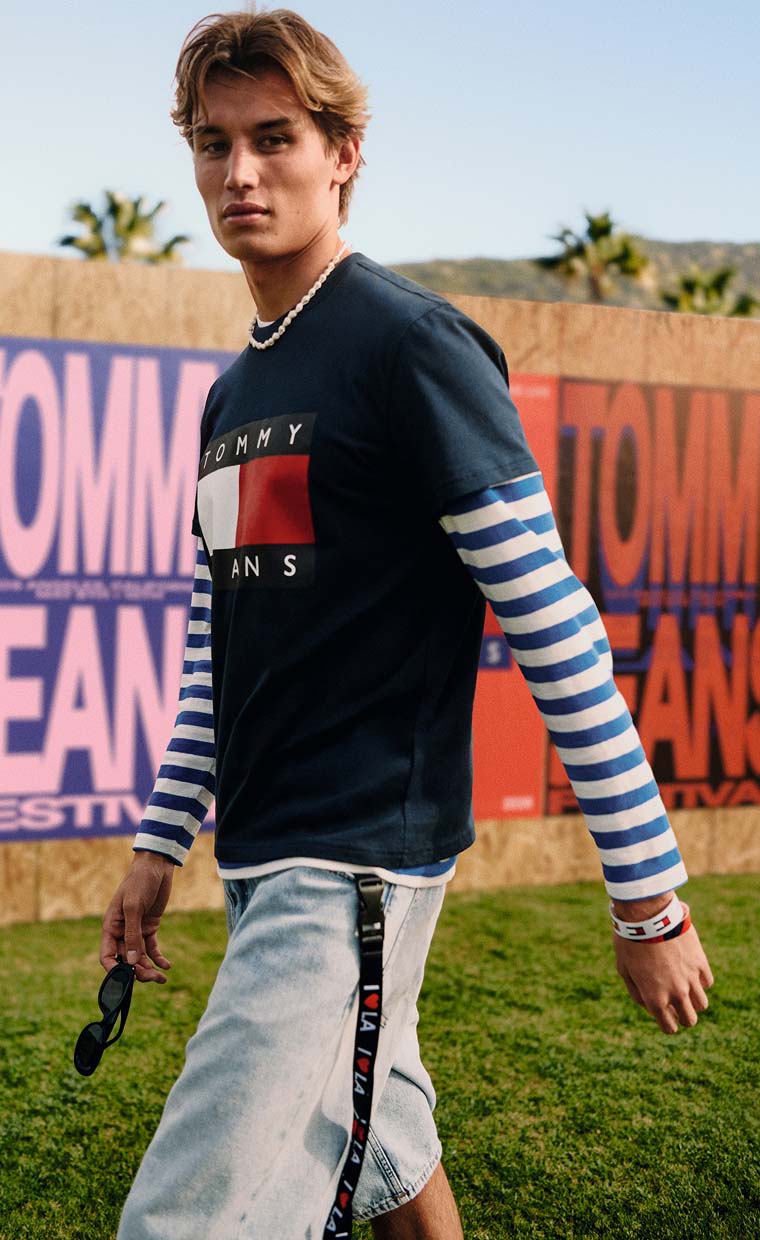 Young man walking outdoors wearing a Tommy Jeans long-sleeve shirt and light jeans.