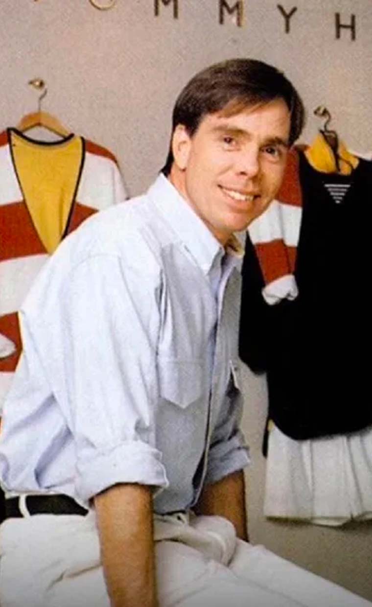 Tommy Hilfiger sitting in front of his outfit designs.