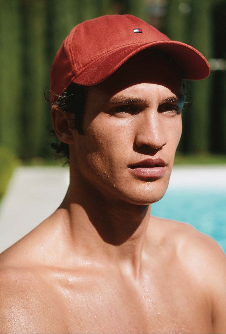 Man wearing a Tommy Hilfiger red cap looking to the side in bright sunlight.