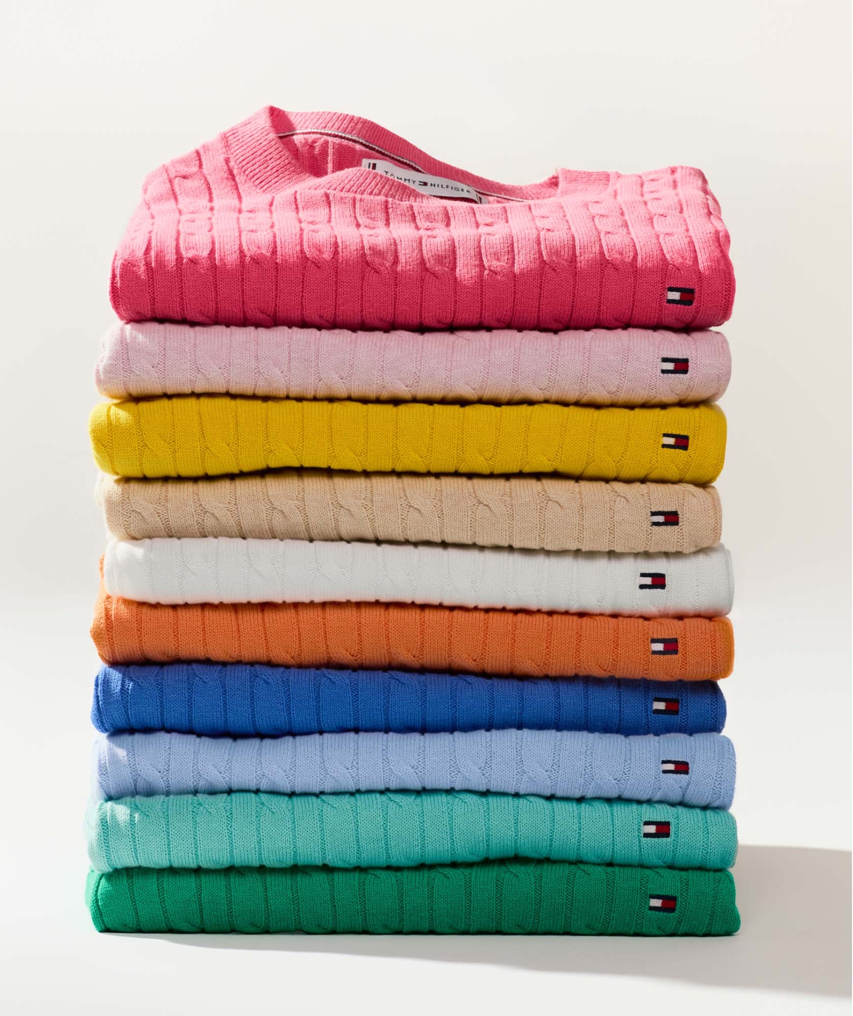 A tall stack of Tommy Hilfiger cable knit sweaters in a wide range of colors.