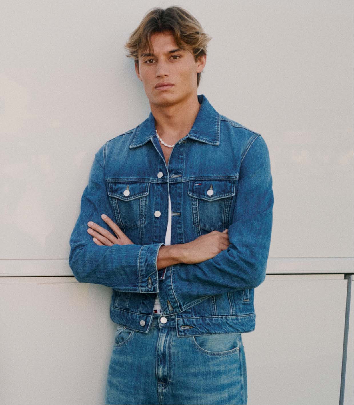 Close up of model adjusting sunglasses wearing a colorblocked Tommy Hilfiger pullover with a large TOMMY logo over a light blue button down shirt.