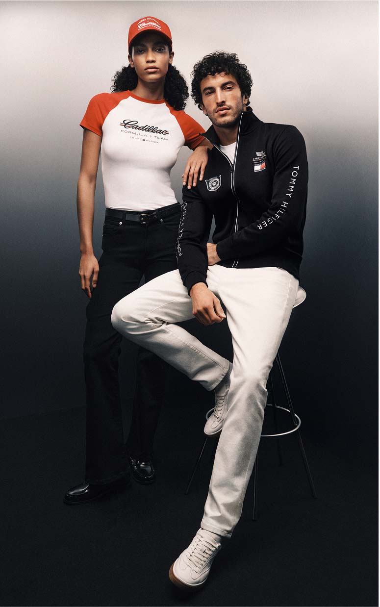 Two models posing in branded racing-inspired outfits, one seated and one standing.