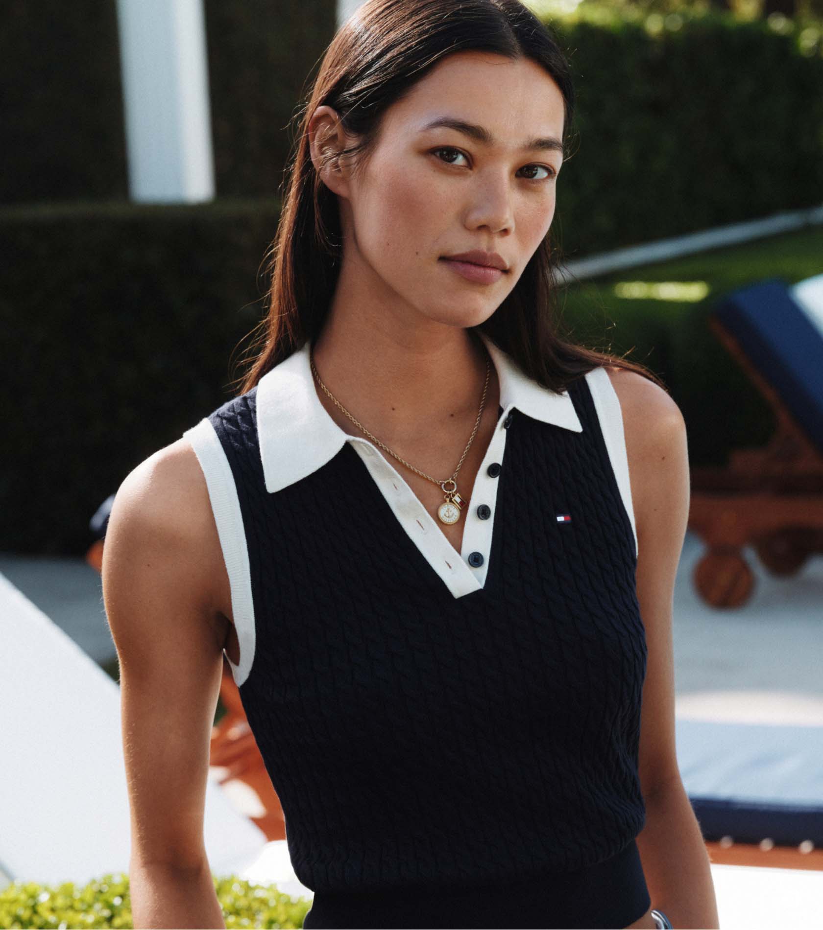 A woman wearing a Tommy Hilfiger sleeveless dark knit top with a white collar, looking confidently at the camera.