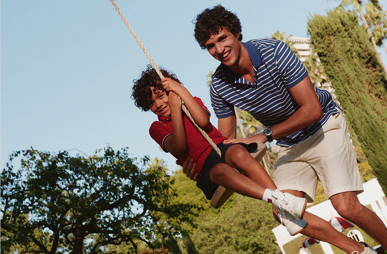 A man and a young boy smiling while holding onto a rope outdoors on a sunny day wearing Tommy Hilfiger outfits.