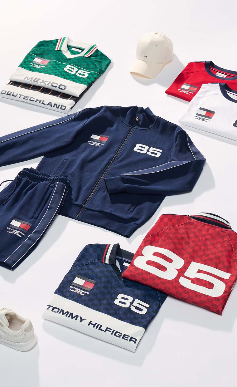 Flat lay of folded Tommy Hilfiger clothing and accessories, including jackets, shirts, and a cap in red, white, blue, and green.