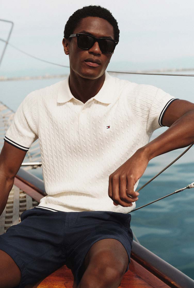 Man sitting on a boat wearing a light-colored Tommy Hilfiger polo shirt and sunglasses, with the ocean behind him.