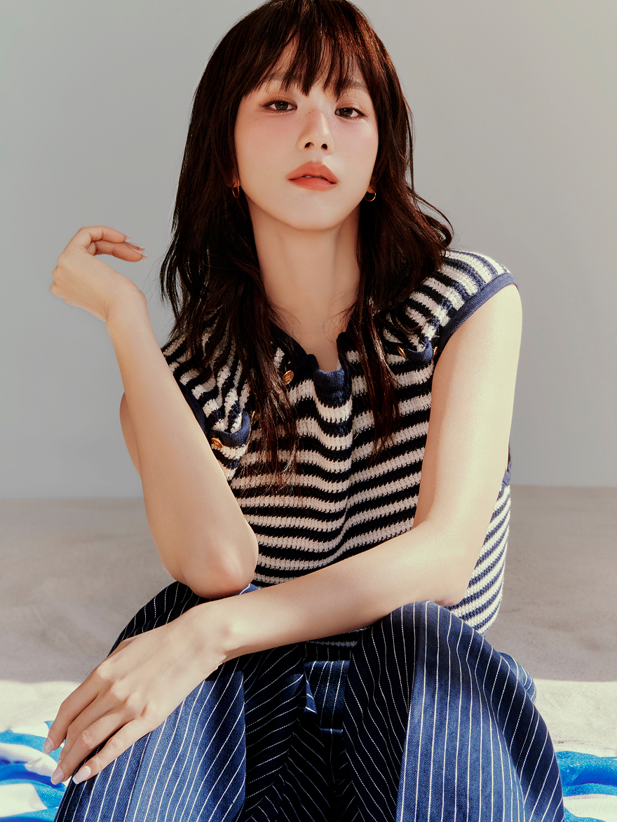 Jisoo sitting and posing in a sleeveless Tommy Hilfiger striped knit top and matching skirt, looking at the camera.
