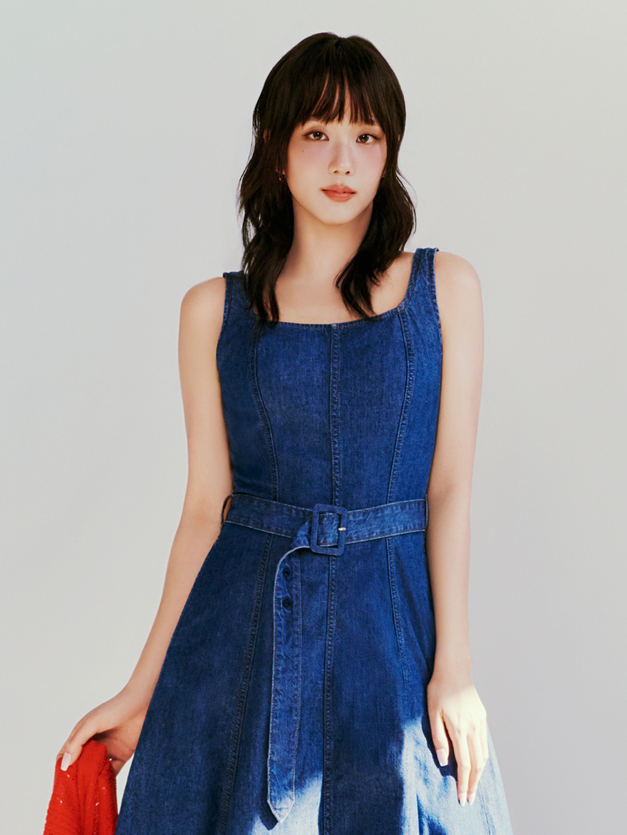 Jisoo standing against a plain background wearing a sleeveless Tommy Hilfiger denim dress, holding a red garment.