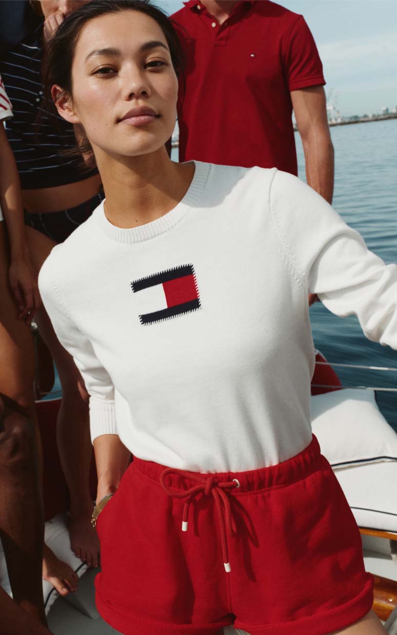 Female model wearing a white Tommy Hilfiger T-shirt tucked into red shorts.