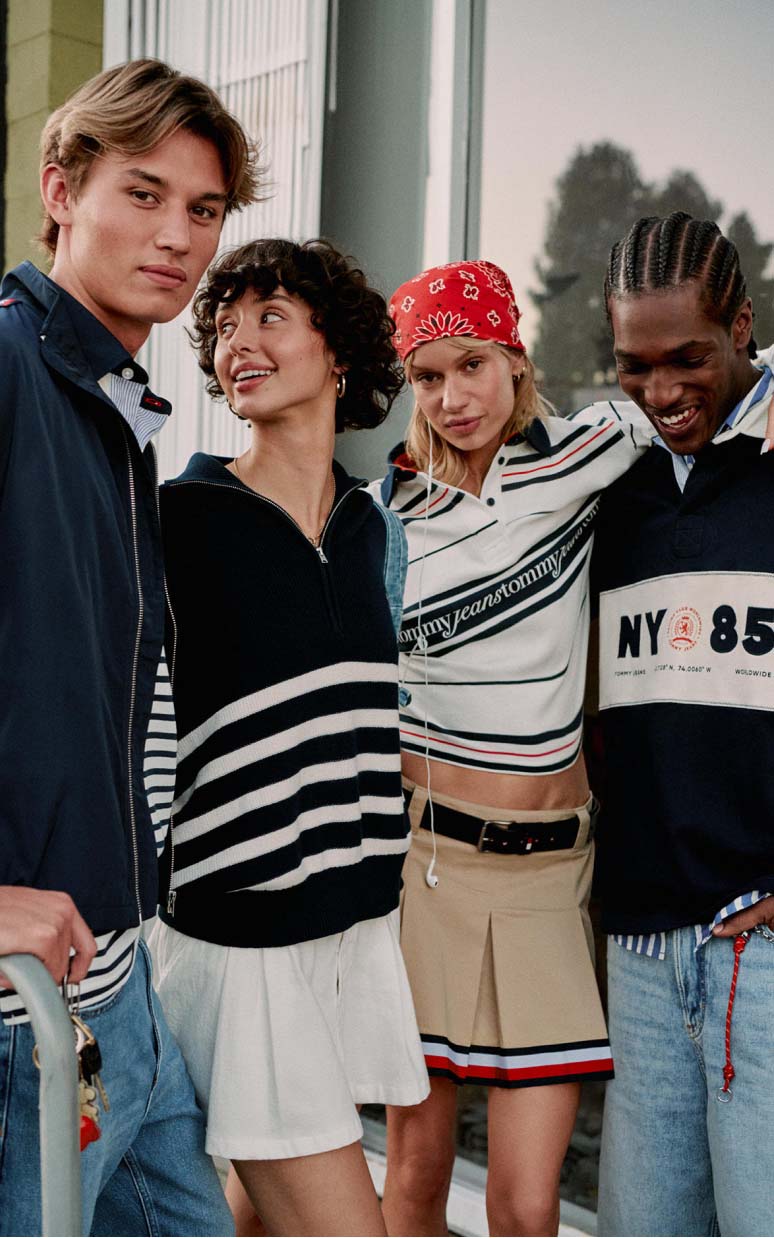 Group of young models wearing preppy striped and layered Tommy Jeans outfits in an urban setting.