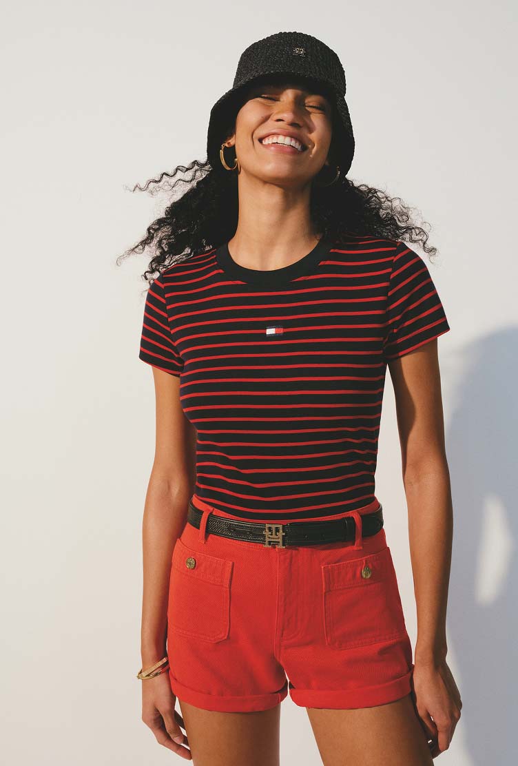 Model wearing a navy and red striped Tommy Hilfiger T-shirt, black bucket hat, and red shorts.