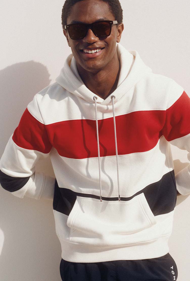 Male model wearing a white Tommy Hilfiger hoodie with bold red and navy stripe detailing.