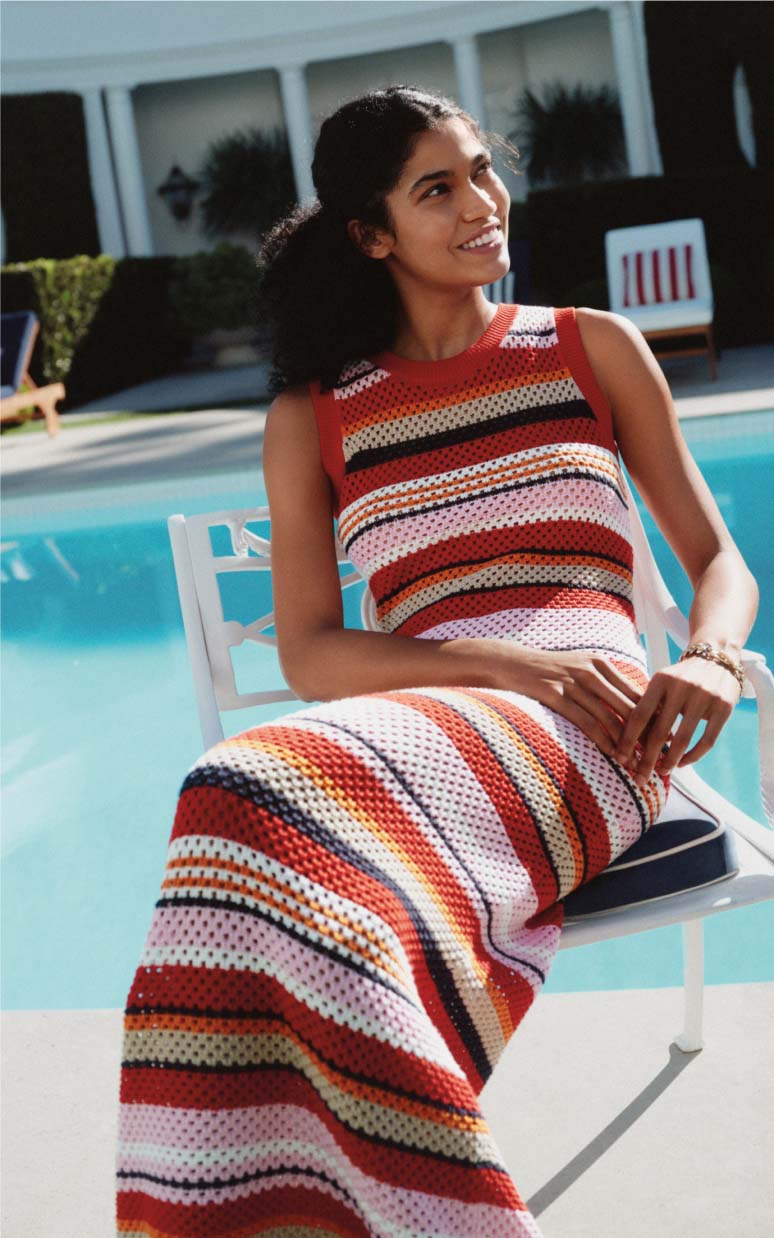 Woman seated poolside wearing a colorful striped Tommy Hilfiger knit dress.