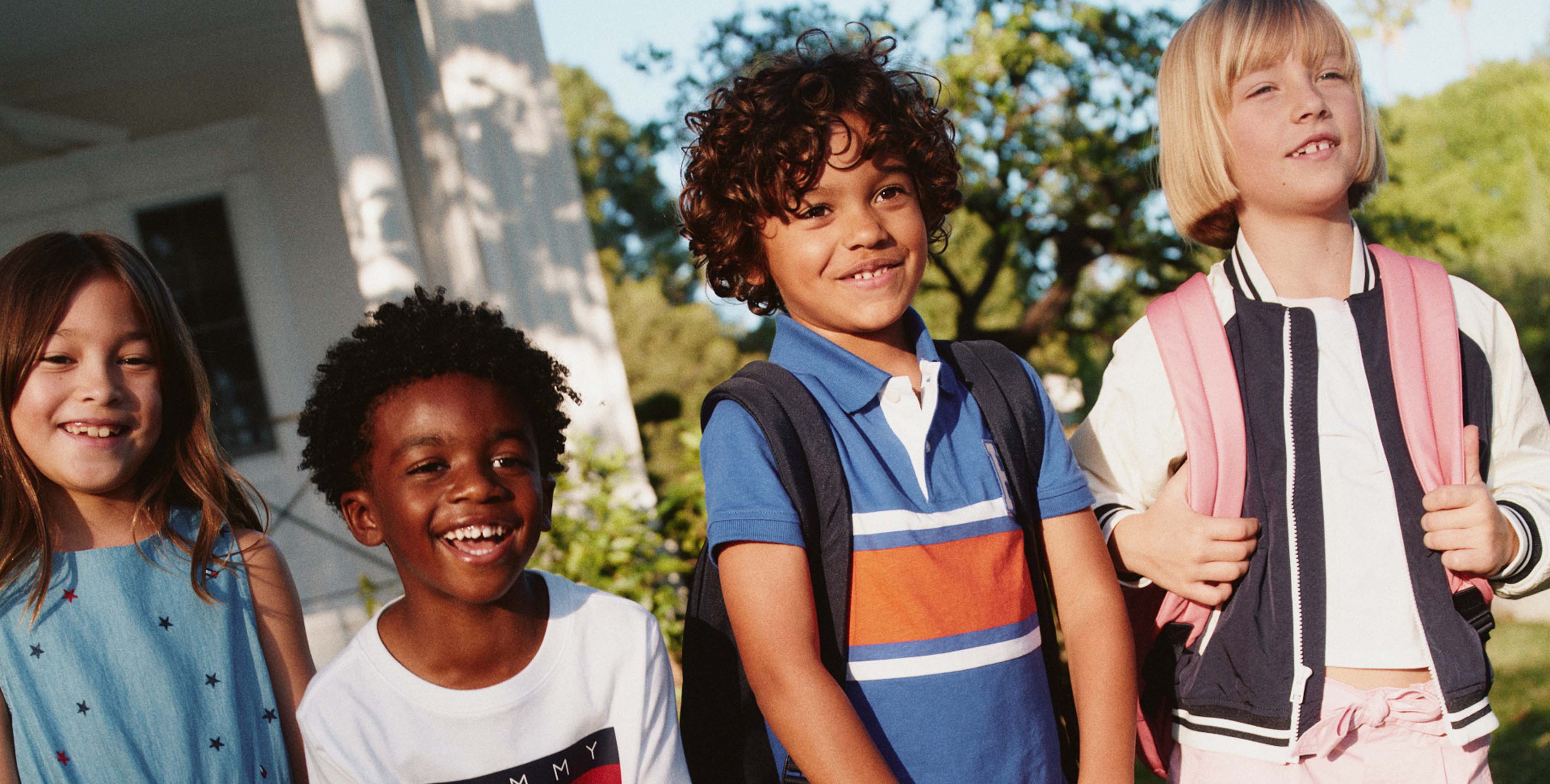 Children outdoors wearing Tommy Hilfiger clothing and backpacks.