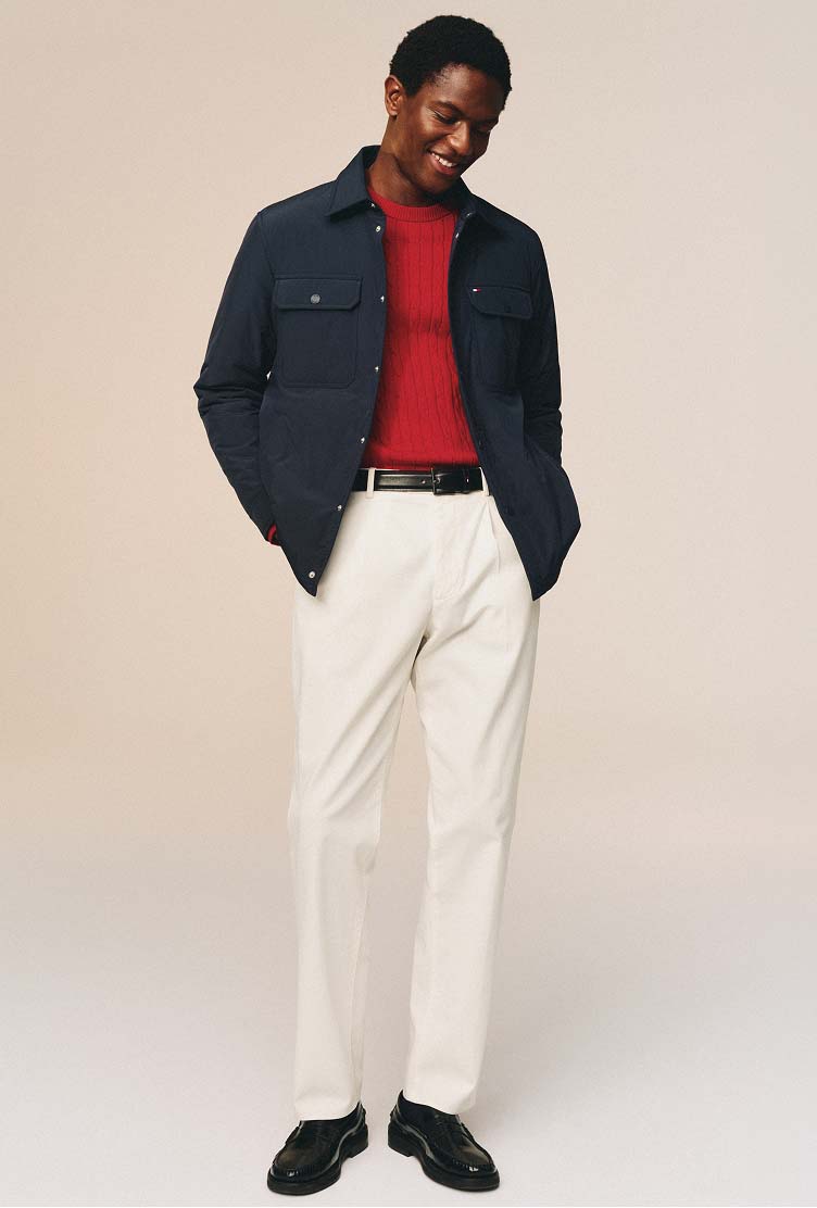Model wearing a Toomy Hilfiger navy jacket, red polo shirt, and relaxed-fit white chinos.
