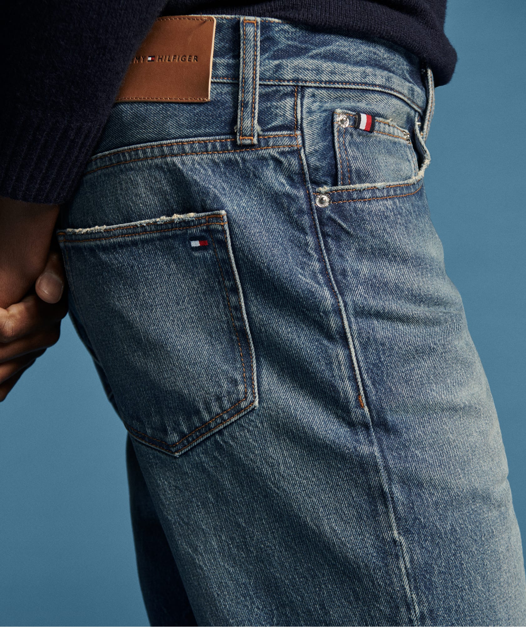 Close-up of the back pocket and waistband of blue denim jeans featuring Tommy Hilfiger branding.