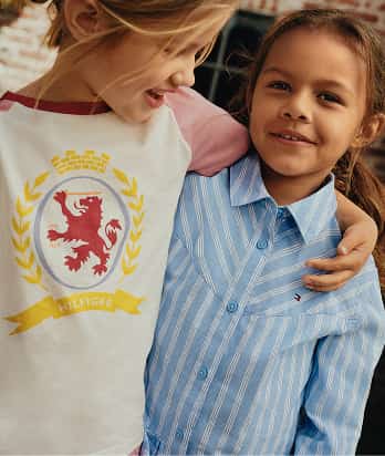 Two children smiling together while wearing casual Tommy Hilfiger outfits outdoors.