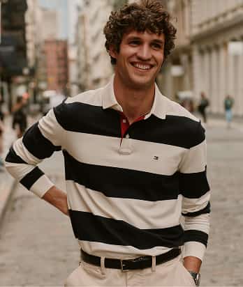 Man wearing a Tommy Hilfiger black and white striped rugby shirt while standing outdoors.