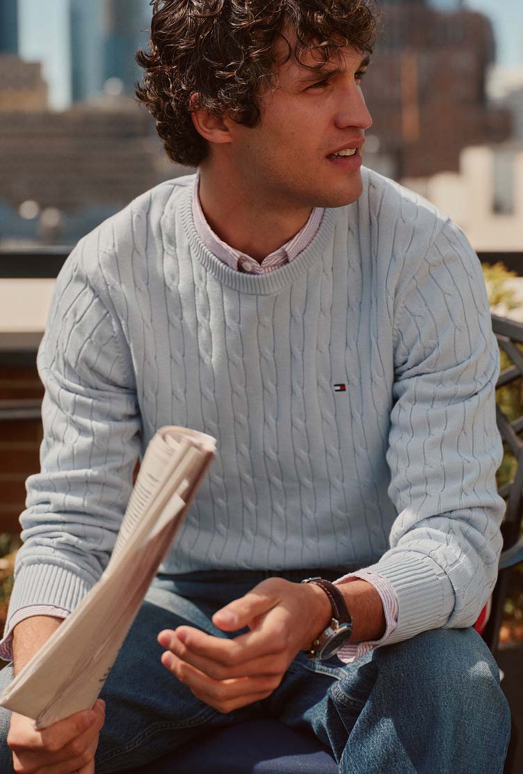 Man wearing a Tommy Hilfiger light blue cable-knit sweater while sitting outdoors.