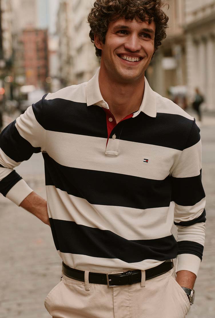 Man wearing a Tommy Hilfiger black and white rugby polo shirt paired with light-colored trousers.