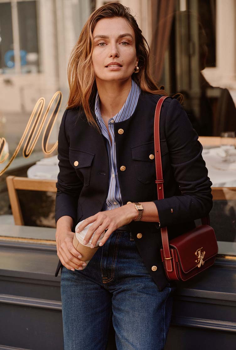 Woman wearing a Tommy Hilfiger navy jacket over a blue shirt with jeans and carrying a burgundy crossbody bag outdoors.