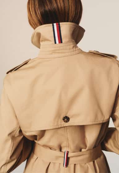 Back view of a person wearing a Tommy Hilfiger beige trench coat with the collar turned up.