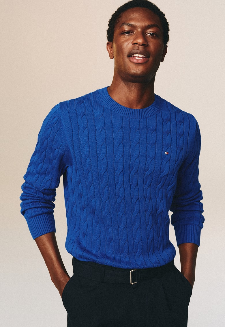 Smiling man wearing a Tommy Hilfiger royal blue cable-knit crewneck sweater.