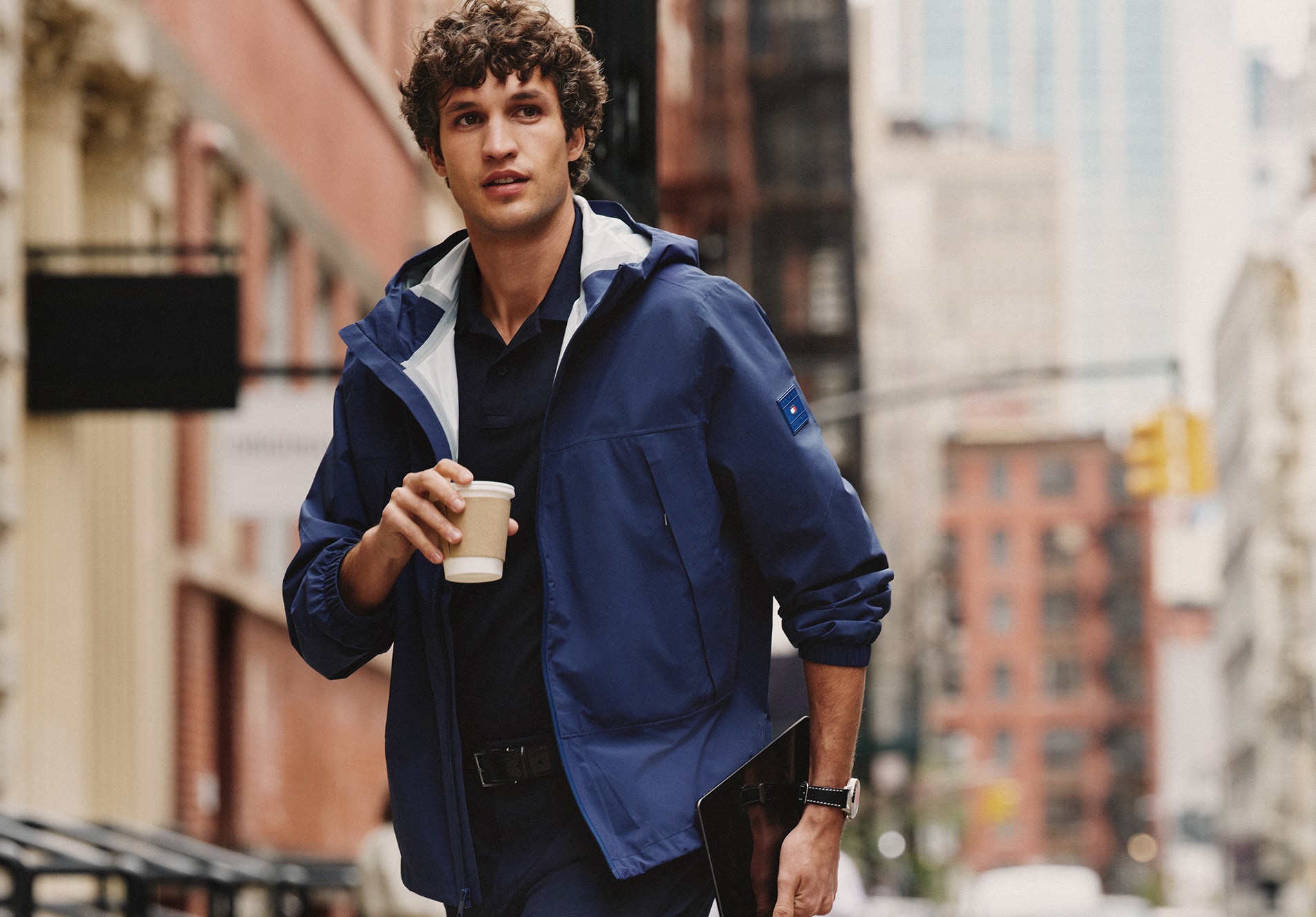 Man walking through a city street wearing a Tommy Hilfiger navy hooded performance jacket.