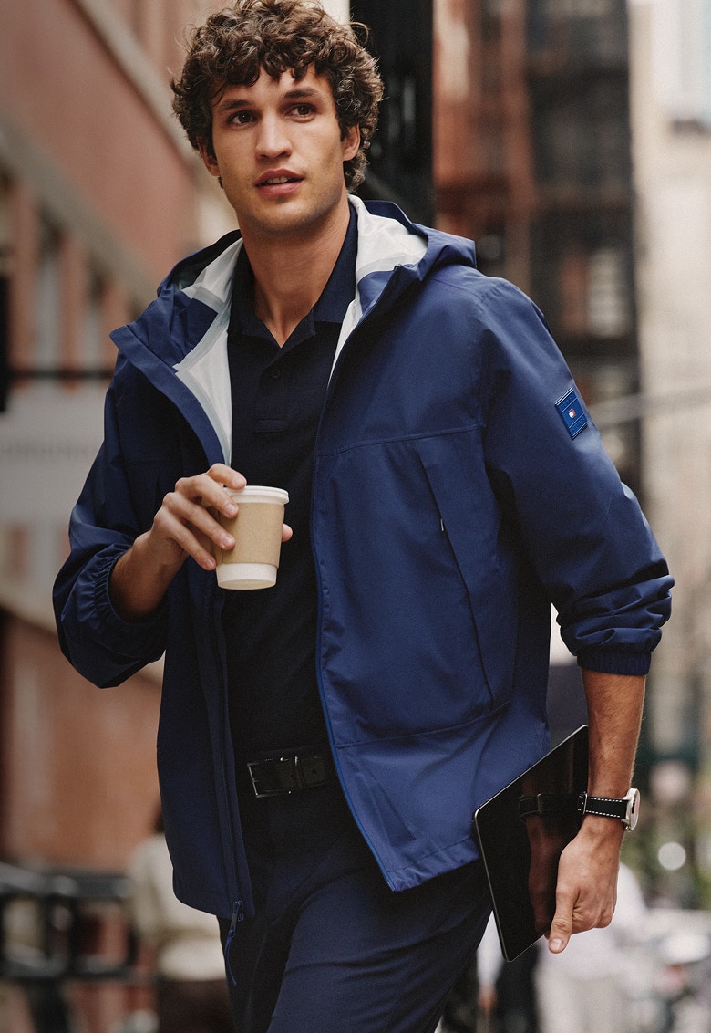Man walking through a city street wearing a Tommy Hilfiger navy hooded performance jacket.