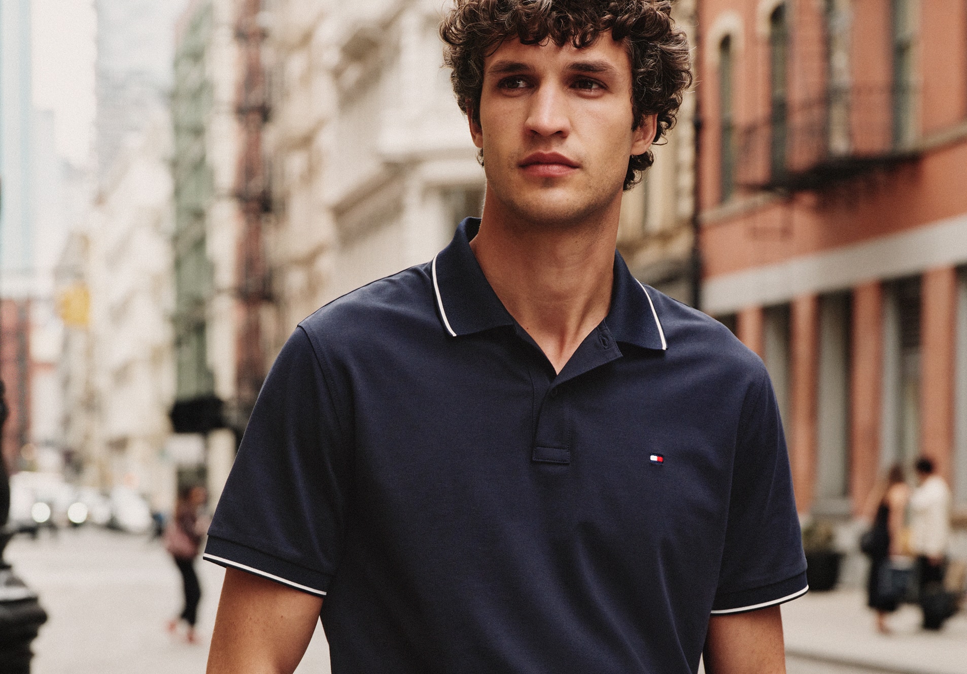 Man standing on a city street wearing a Tommy Hilfiger navy performance polo shirt.