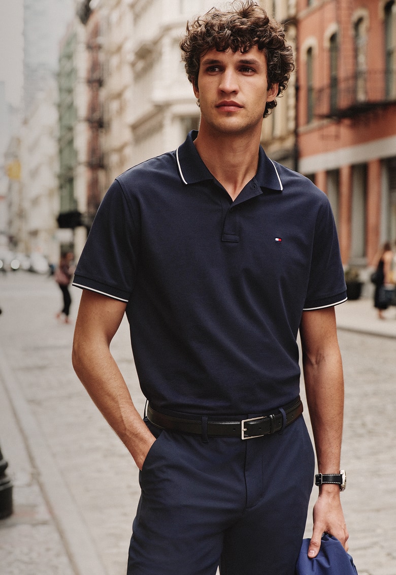 Man standing on a city street wearing a Tommy Hilfiger navy performance polo shirt.