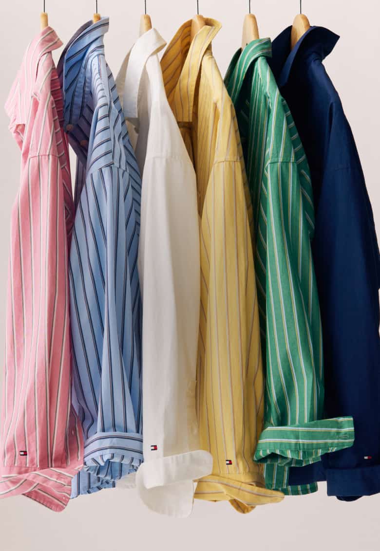 Two images side-by-side: Left side - Model wearing a blue-and-white striped button-down shirt against a red background. Right side - Stack of folded striped button-down shirts in red, yellow, pink, and blue colorways.