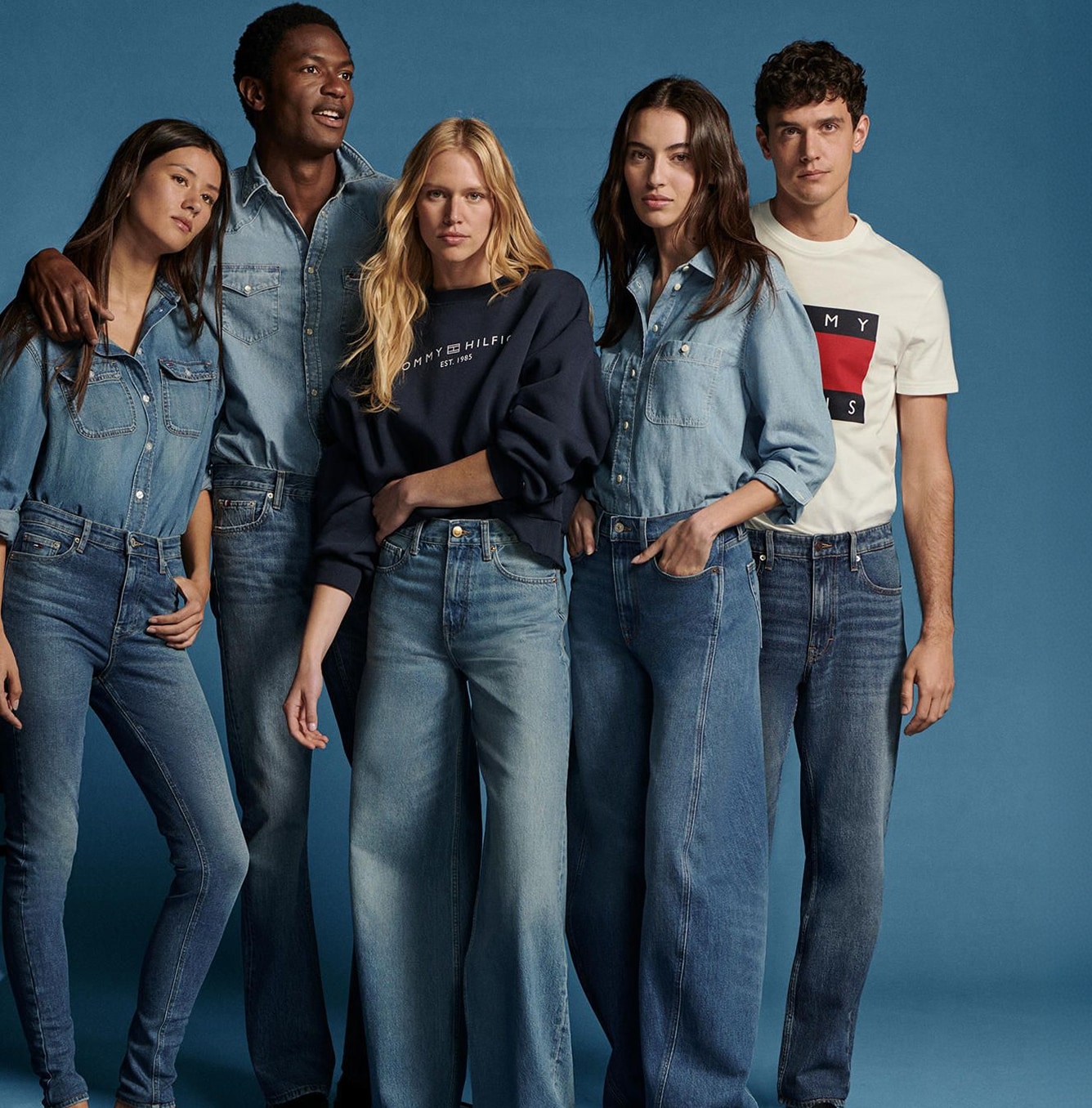 Two models wearing light and dark wash Tommy Hilfiger denim jackets and jeans, posing against a wooden backdrop