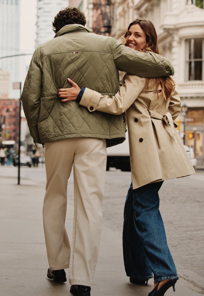Left: Close-up of a man and woman embracing while wearing Tommy Hilfiger lightweight green and beige jackets.
Right: Man and woman standing together on a city street wearing layered Tommy Hilfiger outerwear and casual clothing.