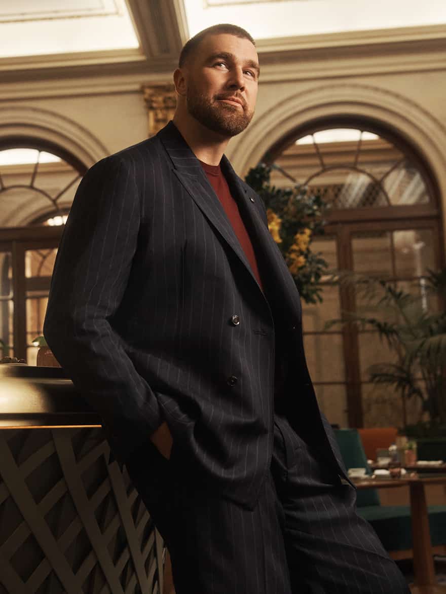Travis Kelce wearing a Tommy Hilfiger navy pinstripe suit with a burgundy sweater.