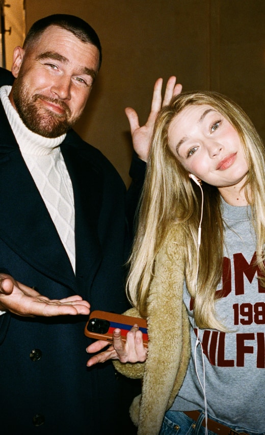 Travis Kelce and Gigi Hadid posing in a Tommy Hilfiger varsity-inspired sweater during an indoor gathering.