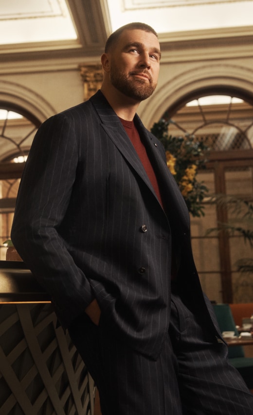 Travis Kelce wearing a Tommy Hilfiger navy pinstripe suit with a burgundy sweater.