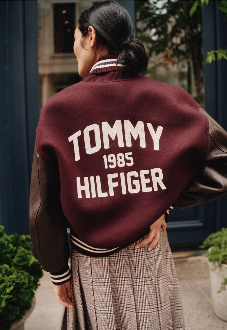 Female model wearing a varsity prep jacket and plaid skirt, new from Tommy Hilfiger.