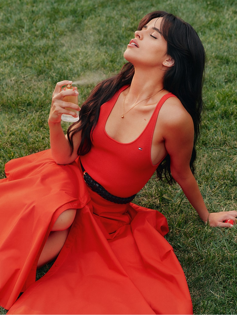 Camila Cabello wearing a Tommy Hilfiger Red dress, holding the new Freedom fragrance.