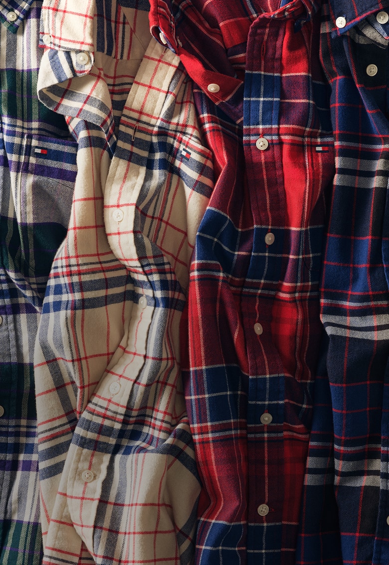 Close-up of layered Tommy Hilfiger flannel button-down shirts in red, navy, cream, and green.